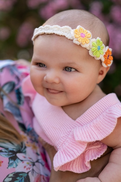 Newborn baby girl with pink knitted clothes and a head accessory among flowers