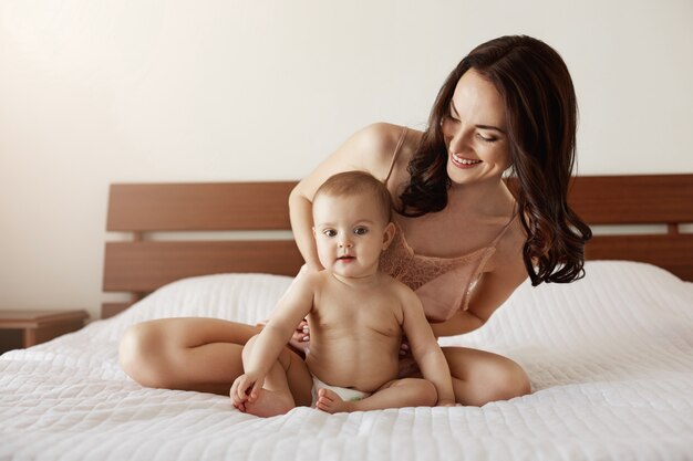 Newborn baby sitting home with her mother playing and smiling. Mom enjoying her motherhood.