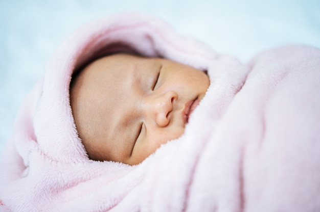 柔らかい​ピンク​の​毛布​で​寝ている​生まれた​ばかり​の​赤ちゃん