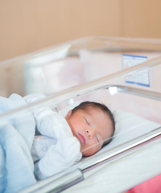 Newborn baby sleeps in hospital crib in newborn clothes