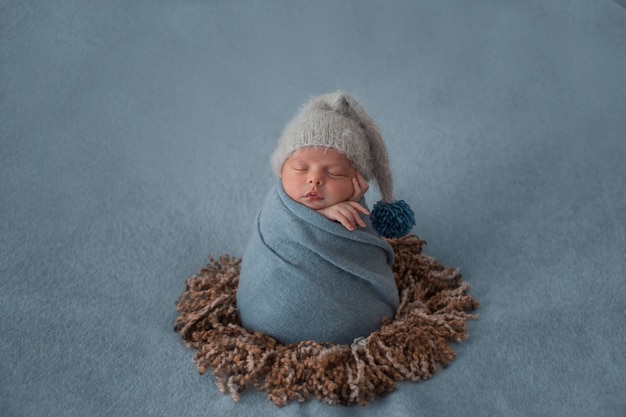Newborn baby with white beret and wrapped with blue shawl.