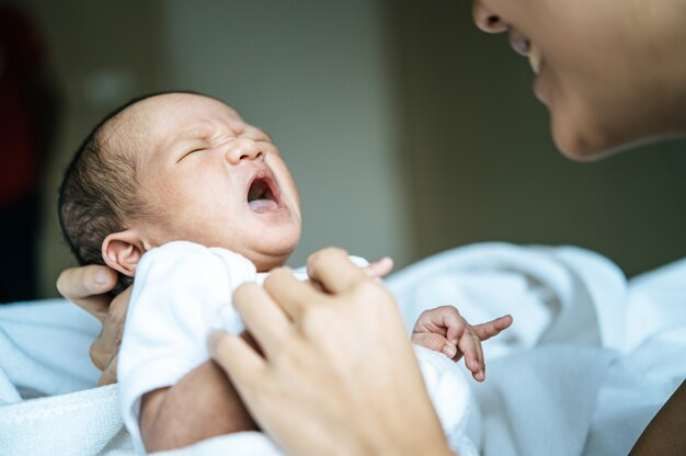 newborn baby wore a white and cried in the arms of the mother