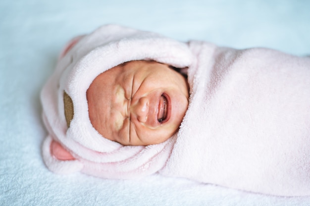 Newborn baby wrapped in a soft pink blanket and crying