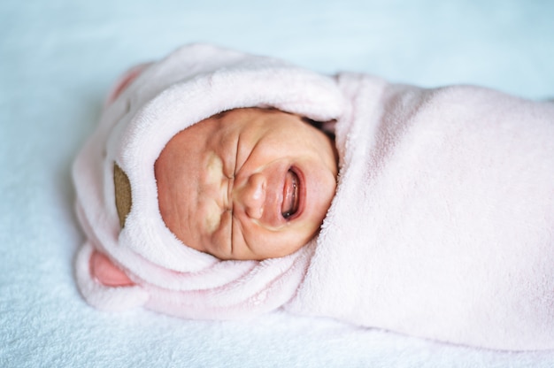 柔らかいピンクの毛布に包まれて泣いている新生児