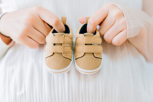 Концепция новорожденного с пальцами, держащими маленькие туфли