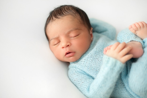 Спящий новорожденный мальчик на белом стуле в симпатичной синей вязаной крючком