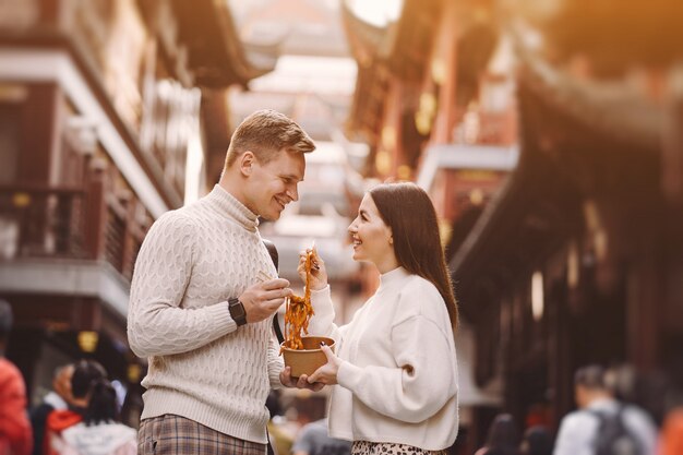 Newlywed couple eating noodles with chopsticks in Shanghai outside a food market