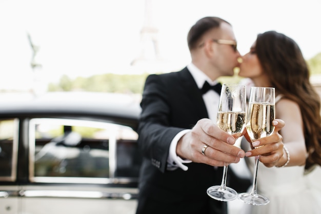 Newlyweds drink champagne standing before a retro car