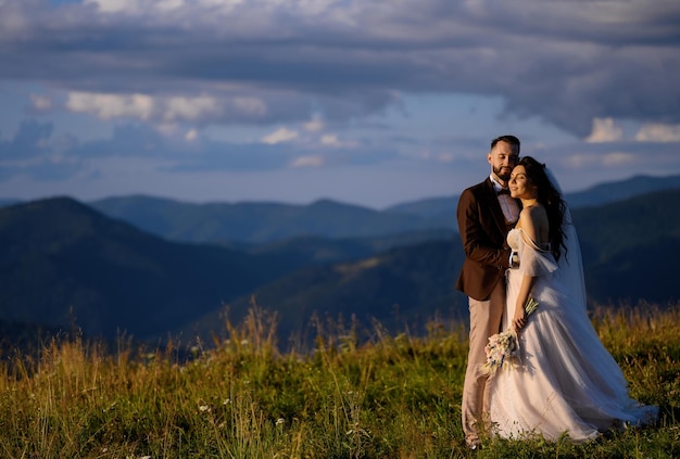 丘の上でポーズをとって夕日を見ている新婚夫婦