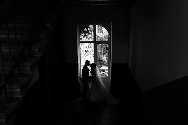 Newlyweds silhouette near a high window in a staircase of old building