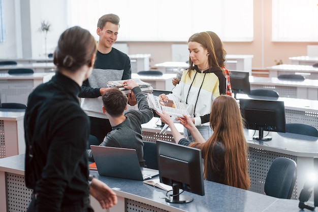 Newspapers in hands. Group of young people in casual clothes working in the modern office