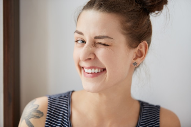 Nice close-up portrait of young European hipster girl with bunch of brown hair and tattoo. Happy tricky cute woman with smiling face