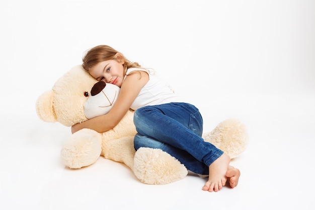 Nice girl lying on floor with toy bear hugging it.