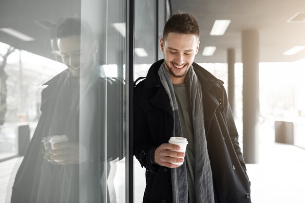 白い紙コップを保持している黒いコートを着た素敵な男性。