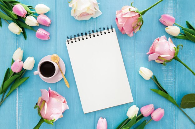 Nice notebook surrounded by tulips and roses on a blue wooden 