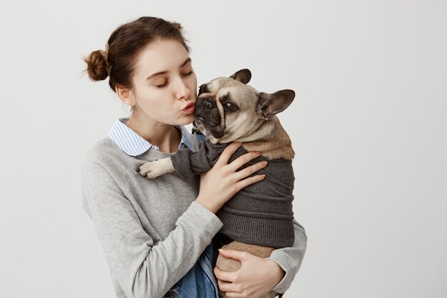 大人の女の子が優しく抱きしめながらかわいい小型犬にキスをするナイスショット。友達と一緒に時間を過ごして抱きしめる犬とその飼い主の肖像画。愛情の表示