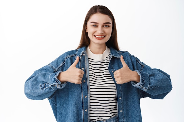 Nice work, great choice. Smiling woman shows thumbs up and looking happy or pleased, recommend or approve something, praise excellent awesome job, standing proud and satisfied on white background