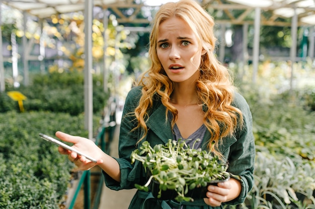 Nice young girl, with light red hair and green eyes, dressed in dark green dress, posing while holding her smartphone in her hands