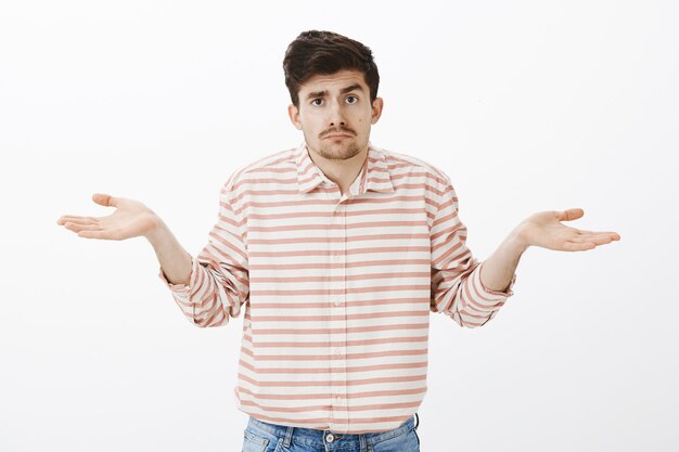 No clue, no guesses. Portrait of gloomy unsure boyfriend with moustache, shrugging with spread palms, being confused and unaware what is happening, standing clueless