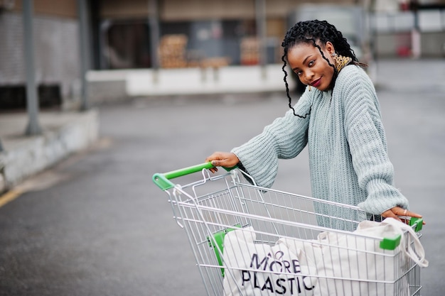 ショッピングカートのトロリーとエコバッグを持ったプラスチック製のアフリカの女性が屋外市場を提起することはもうありません