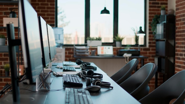 No people at desk with multiple computers in call center office, used by telemarketing agents to answer phone calls on helpline. Empty space with technology to give assistance at customer care.