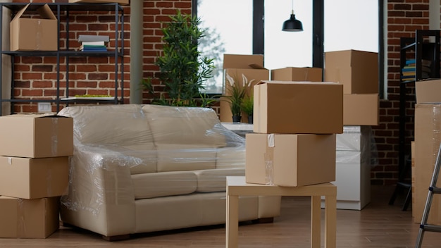 No people in living room interior to move in with carton boxes, empty real estate property full of cardboard packing storage cargo. Nobody in apartment for relocation and moving day.