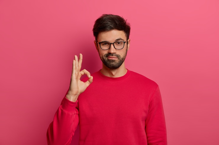 Free Photo no problem concept. bearded man makes okay gesture, has everything under control, all fine gesture, wears spectacles and jumper, poses against pink wall, says i got this, guarantees something