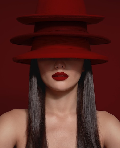 Бесплатное фото Нет узнаваемой модели с половиной лица, закрытой красными шляпами, и яркой матовой красной помадой красное фоновое изображение с красными губами