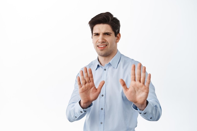 No thank you Disgusted and reluctant man shaking hands to refuse rejecting bad offer frowning from cringe standing bothered against white background