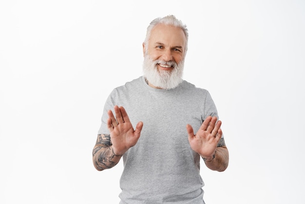 No thank you Smiling happy old guy with tattoos shaking hands to refuse rejecting offer politely decline something standing in grey tshirt against white background