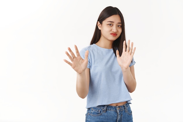 No thanks I pass Indifferent asian reluctant girl refusing unintersting offer smirking displeased raise hands stop enough no gesture shaking palms refusal rejecting awful offer white background