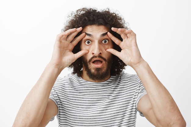 Assolutamente no, non posso credere alla mia vista. ragazzo divertente stupito scioccato con barba e capelli ricci, allungando le palpebre con le dita e fissando con gli occhi spuntati