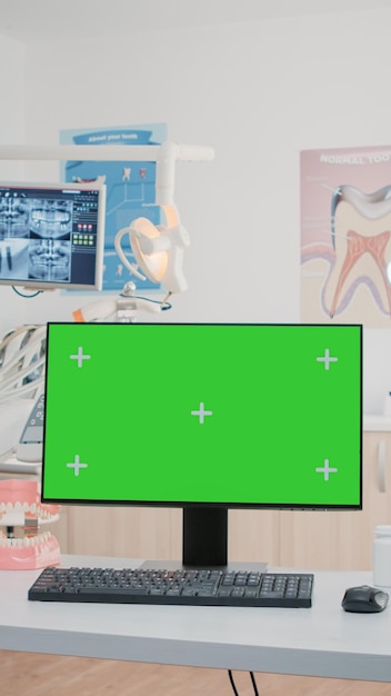 歯のケアのためのコンピュータの緑色の画面を備えた歯科用キャビネットには誰もいません。孤立した背景とクロマキーのモニターにモックアップテンプレートを持つ空の歯科医院。口腔ケアと歯列