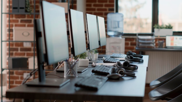 Nobody in empty call center workstation with computers and audio instruments. No people at customer service office desks with telecommunications technology, offering helpline assistance.