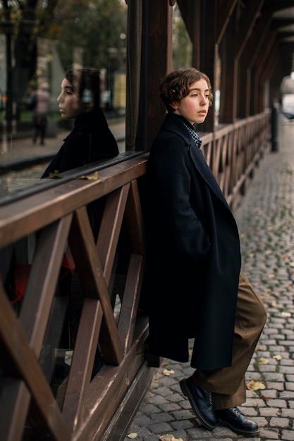 non binary person standing next to wooden house