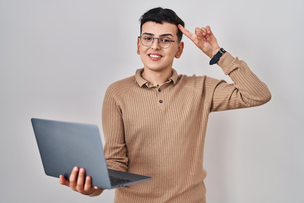 Free photo non binary person using computer laptop smiling pointing to head with one finger, great idea or thought, good memory