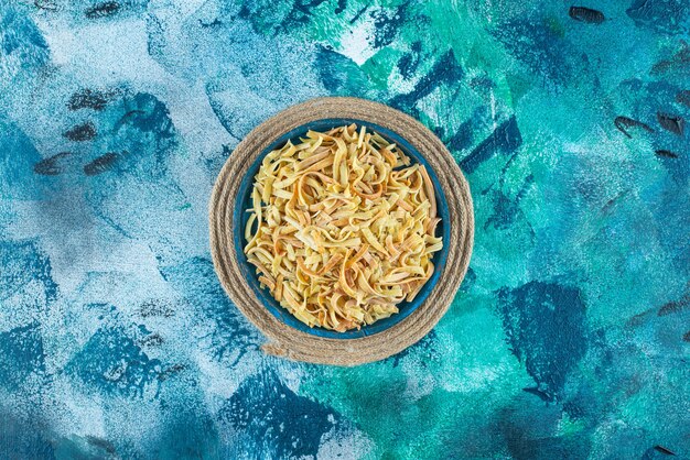 Noodle in a bowl on trivet on blue.