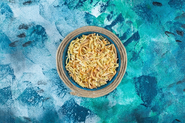 Noodle in a bowl on trivet on blue.