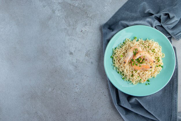 Noodle and shrimp on a plate on a pieces of fabric, on the marble background. 
