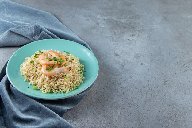 Noodle and shrimp on a plate on a pieces of fabric, on the marble background. 