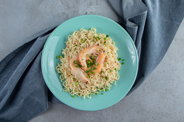 Noodle and shrimp on a plate on a pieces of fabric, on the marble surface.