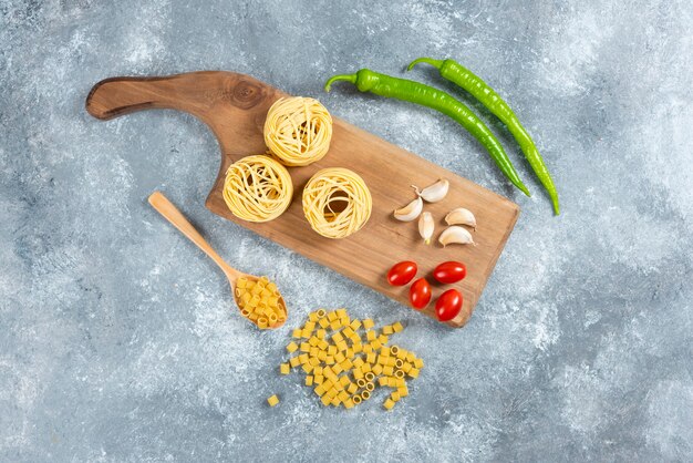 Tagliatelle, aglio e pomodori su tavola di legno.