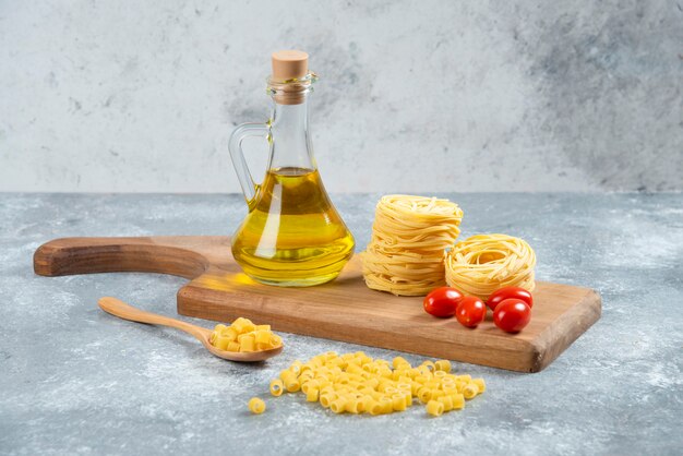 Noodles, olive oil and tomatoes on wooden board.