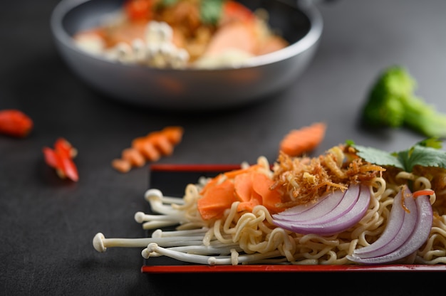 黒いセメント表面に食材を使った木製のトレイでスパイシーな麺。