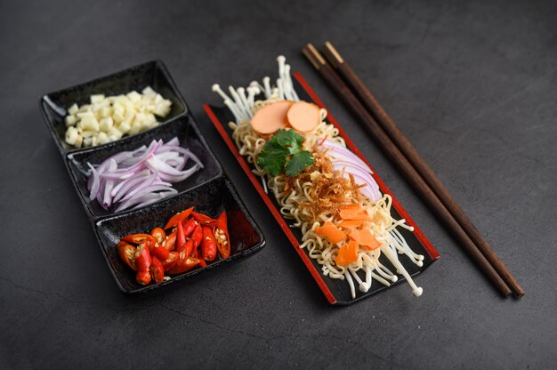 Noodles spicy in Wooden tray with ingredients on black cement surface.