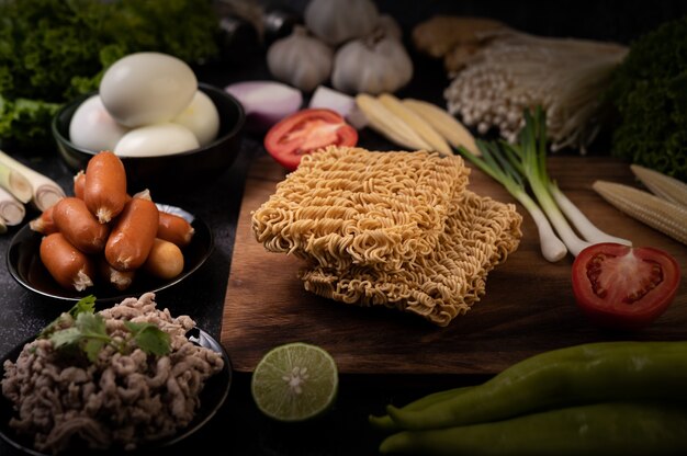 Noodles on a wooden cutting board with tomato, lime, spring onion, chili and baby corn