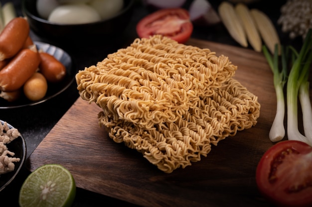 Free photo noodles on a wooden cutting board with tomato, lime, spring onion, chili and baby corn
