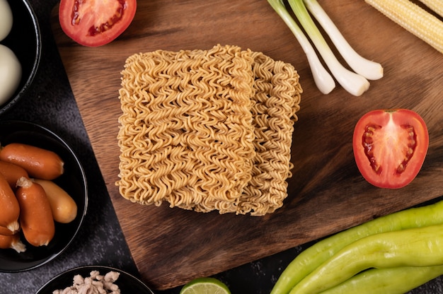 Noodles on a wooden cutting board with tomato, lime, spring onion, chili and baby corn