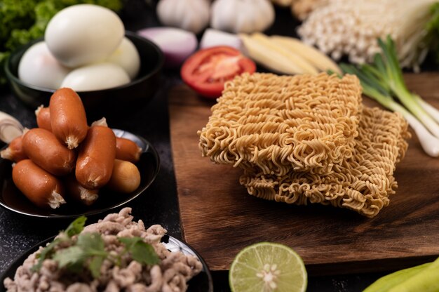 Noodles on a wooden cutting board with tomato, lime, spring onion, chili and baby corn