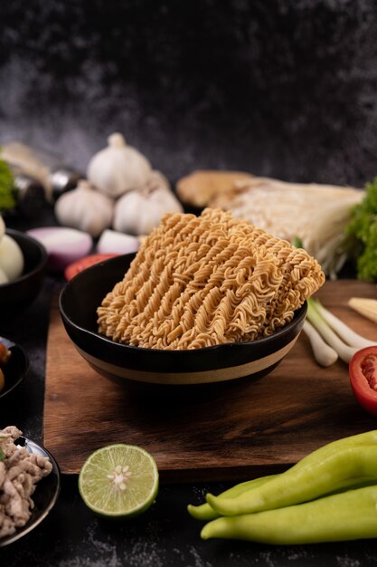 Noodles on a wooden cutting board with tomato, lime, spring onion, chili and baby corn